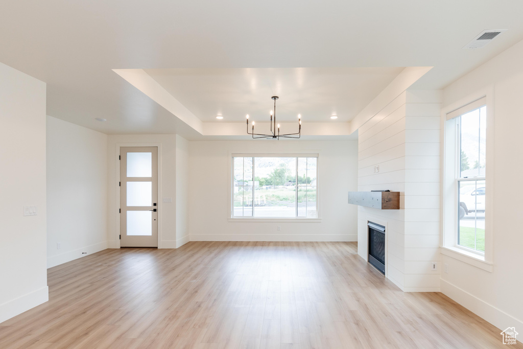 Unfurnished living room featuring a fireplace, plenty of natural light, light hardwood / wood-style floors, and a notable chandelier