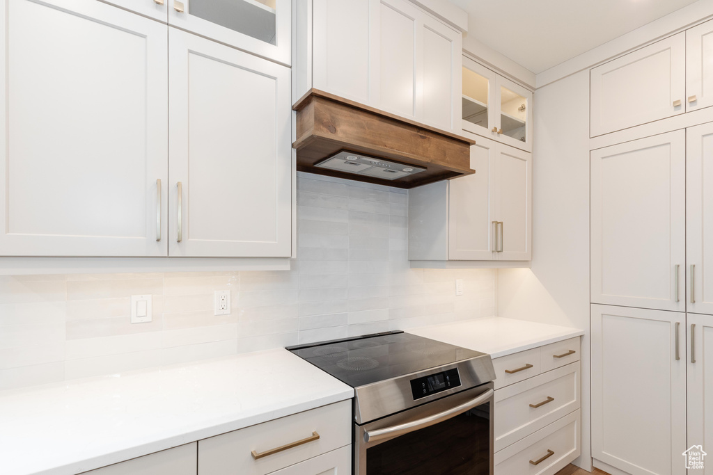 Kitchen featuring custom range hood, stainless steel range with electric stovetop, white cabinets, and backsplash