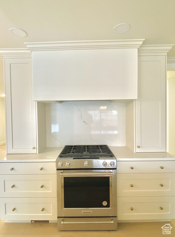 Kitchen with custom range hood, backsplash, gas range, and white cabinets