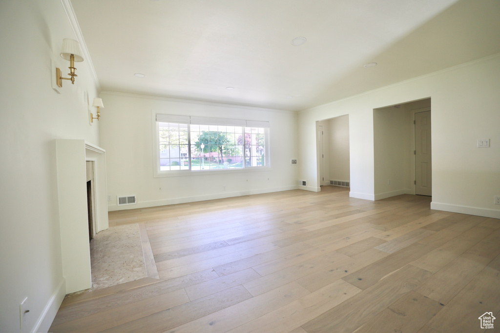 Unfurnished living room featuring light wood-type flooring and ornamental molding