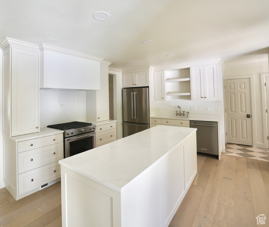 Kitchen featuring white cabinets, sink, stainless steel appliances, light stone countertops, and light hardwood / wood-style floors