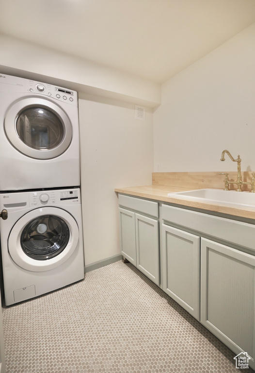 Washroom featuring cabinets, sink, and stacked washer and dryer