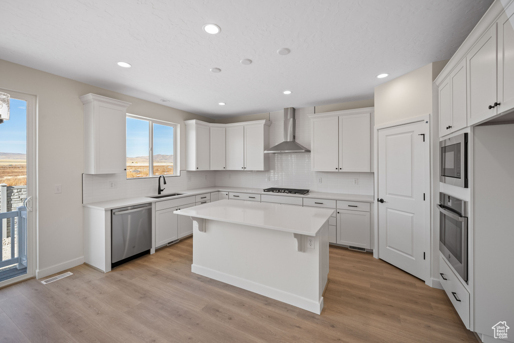 Kitchen with white cabinets, appliances with stainless steel finishes, sink, and wall chimney range hood