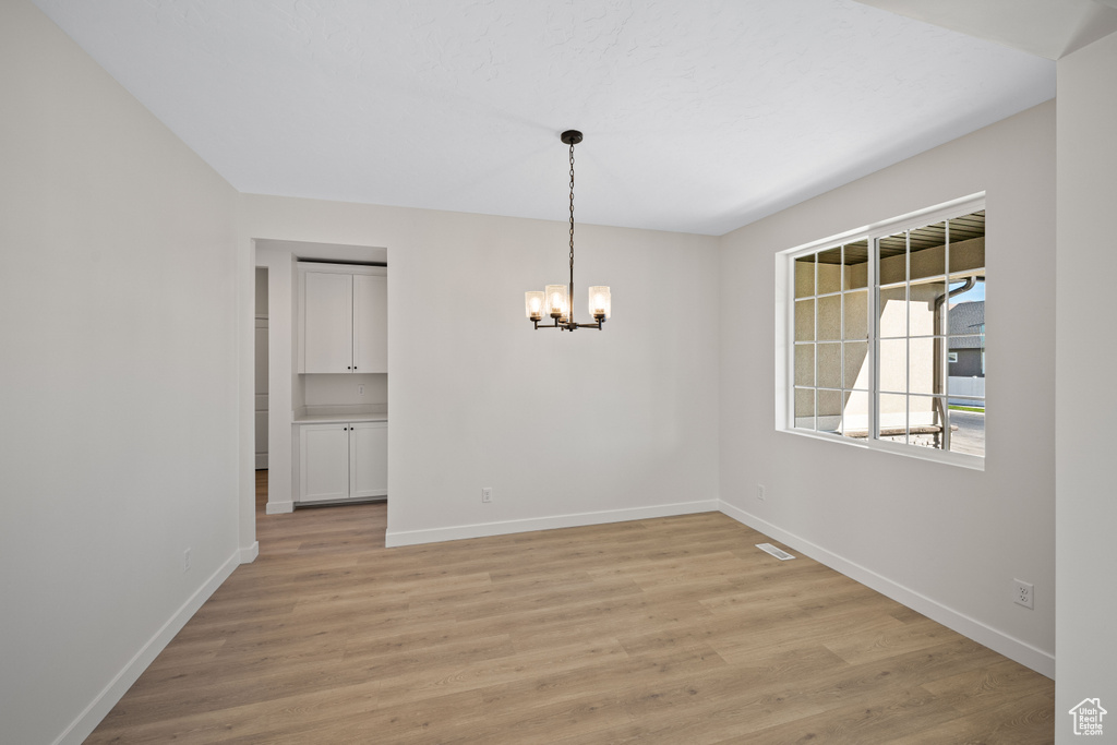 Empty room with an inviting chandelier and light hardwood / wood-style floors