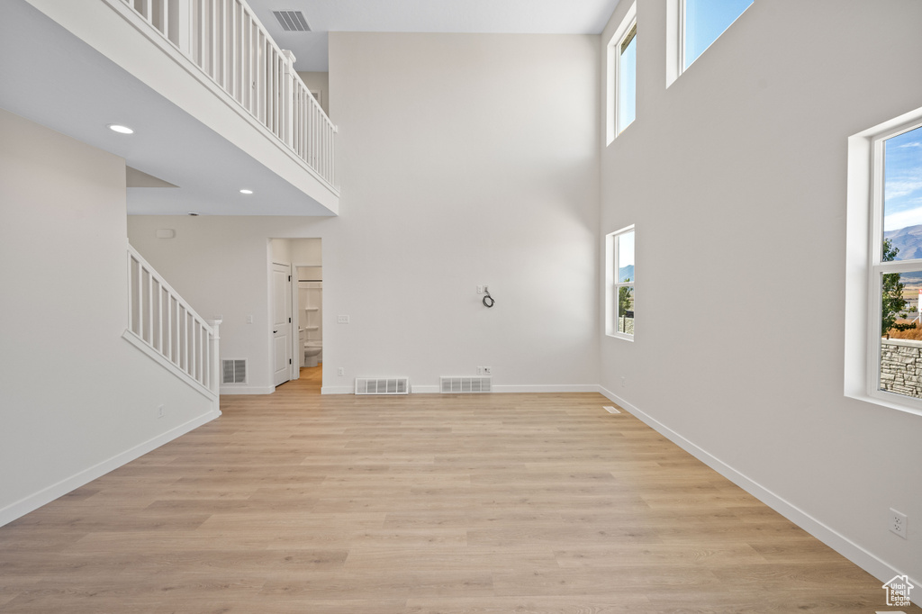 Unfurnished living room featuring light wood-type flooring and a high ceiling