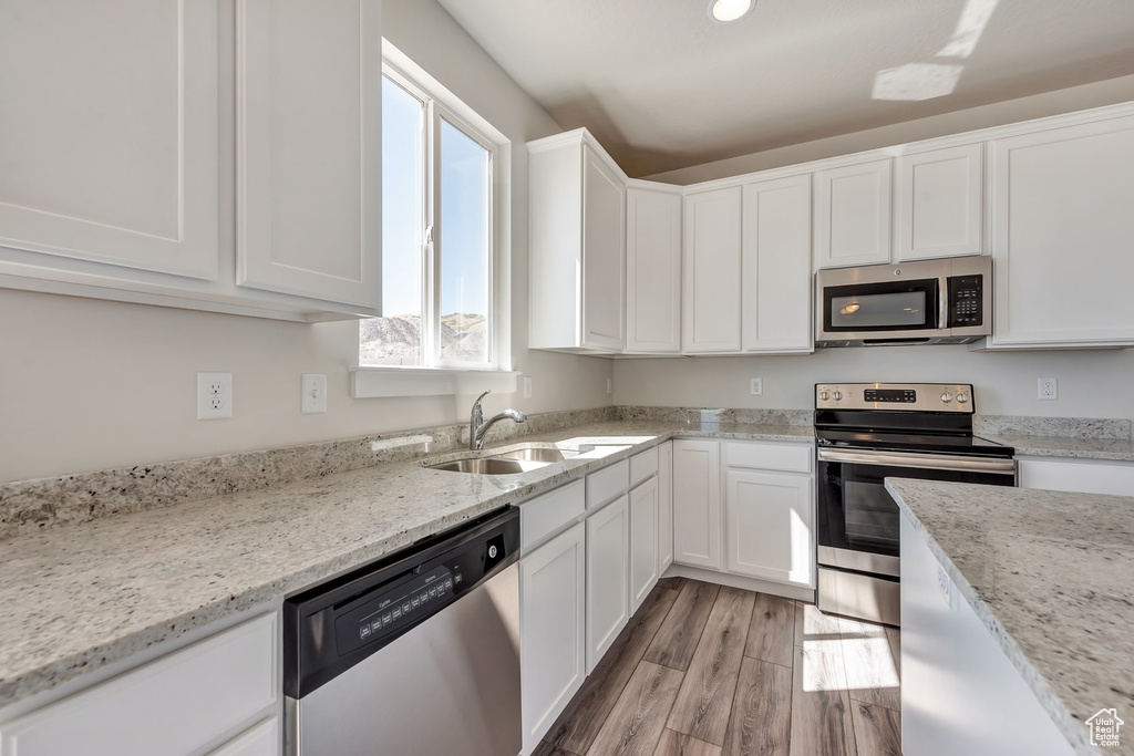 Kitchen featuring appliances with stainless steel finishes, light wood-type flooring, sink, and white cabinets