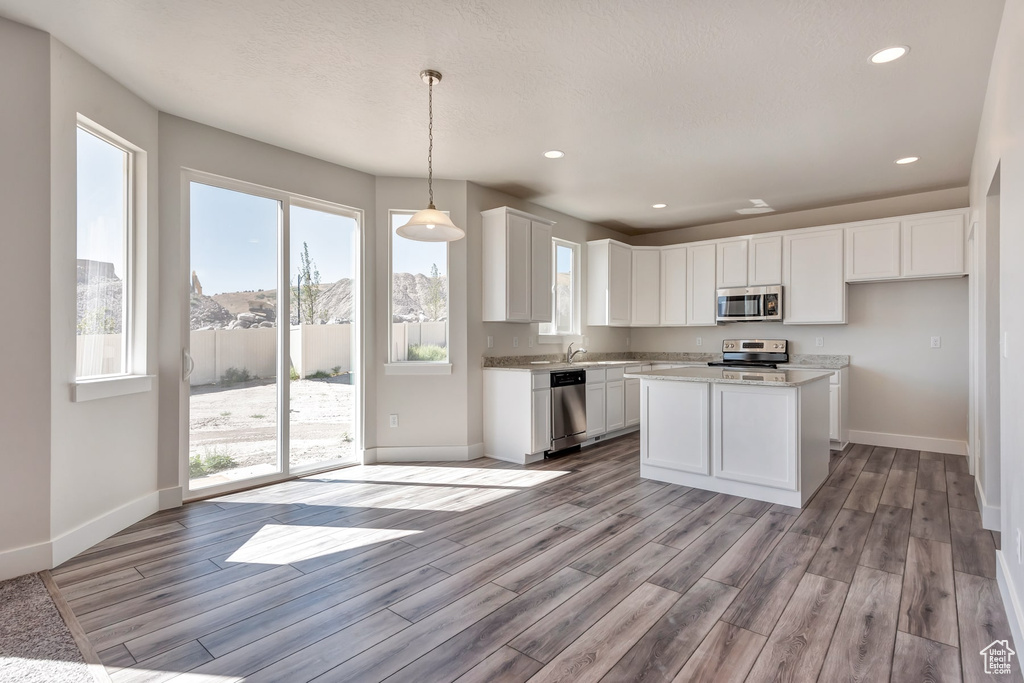 Kitchen with a kitchen island, decorative light fixtures, white cabinetry, stainless steel appliances, and light hardwood / wood-style floors