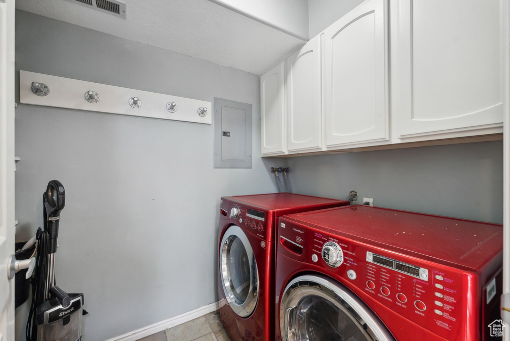 Washroom with light tile patterned flooring, electric panel, washer and dryer, and cabinets