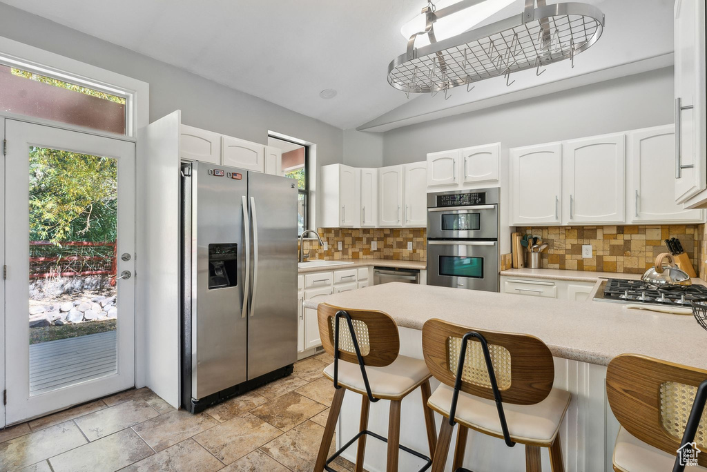 Kitchen with decorative backsplash, white cabinets, appliances with stainless steel finishes, and a kitchen breakfast bar