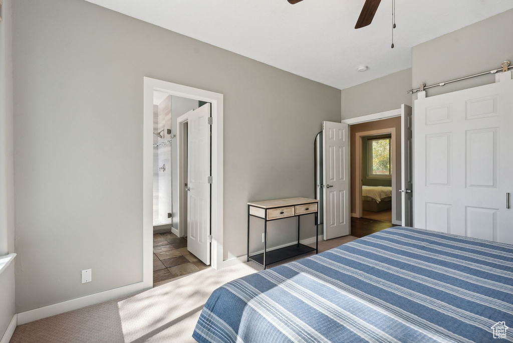 Carpeted bedroom with a barn door, ceiling fan, and ensuite bath