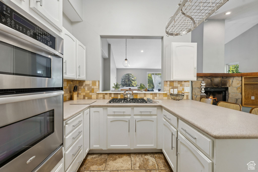 Kitchen with stainless steel appliances, kitchen peninsula, decorative light fixtures, and a fireplace