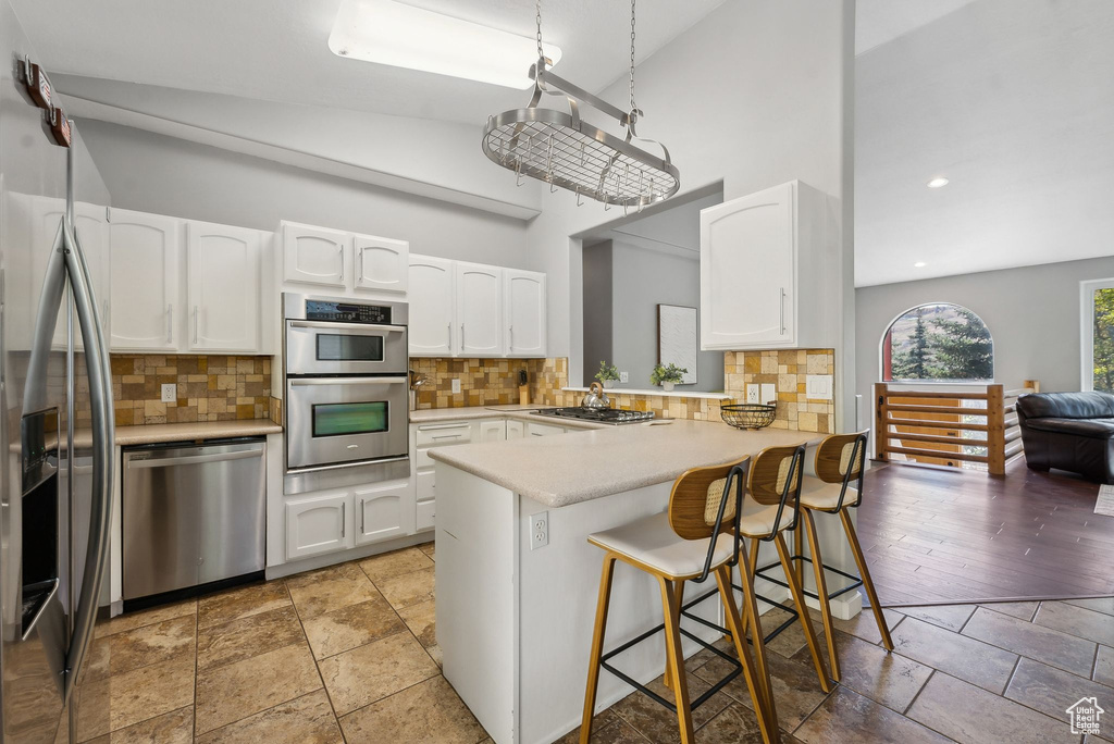 Kitchen featuring a breakfast bar, vaulted ceiling, stainless steel appliances, kitchen peninsula, and white cabinets