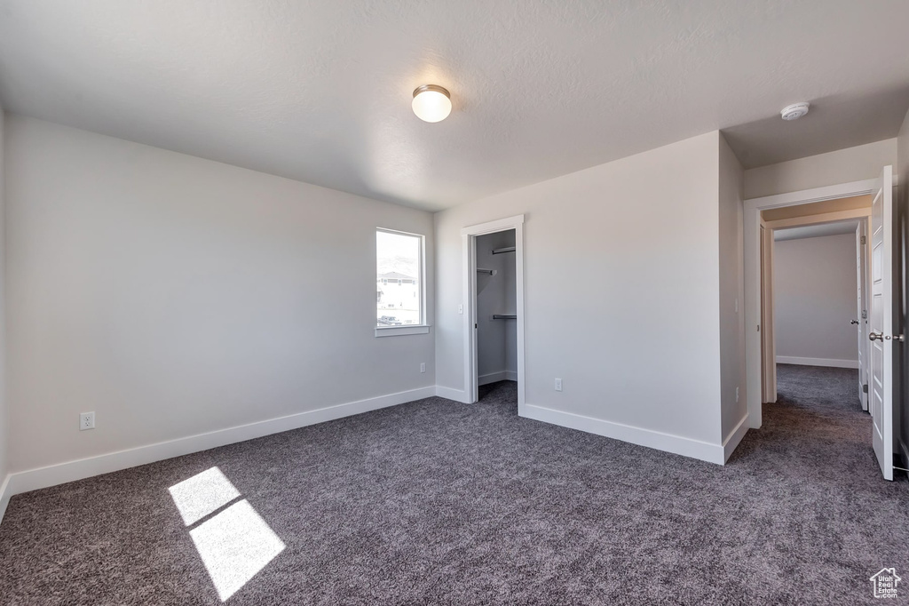 Unfurnished bedroom featuring a spacious closet, a closet, dark colored carpet, and a textured ceiling