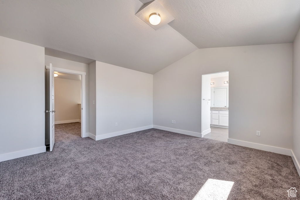 Unfurnished bedroom with ensuite bathroom, vaulted ceiling, and light colored carpet