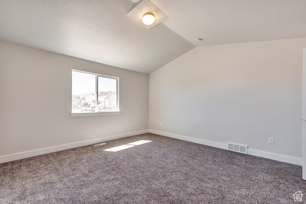 Carpeted empty room with vaulted ceiling and a textured ceiling