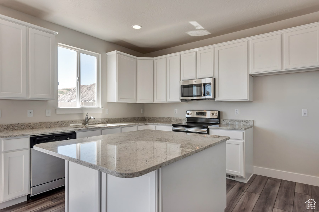 Kitchen with white cabinets, appliances with stainless steel finishes, dark hardwood / wood-style flooring, and a center island