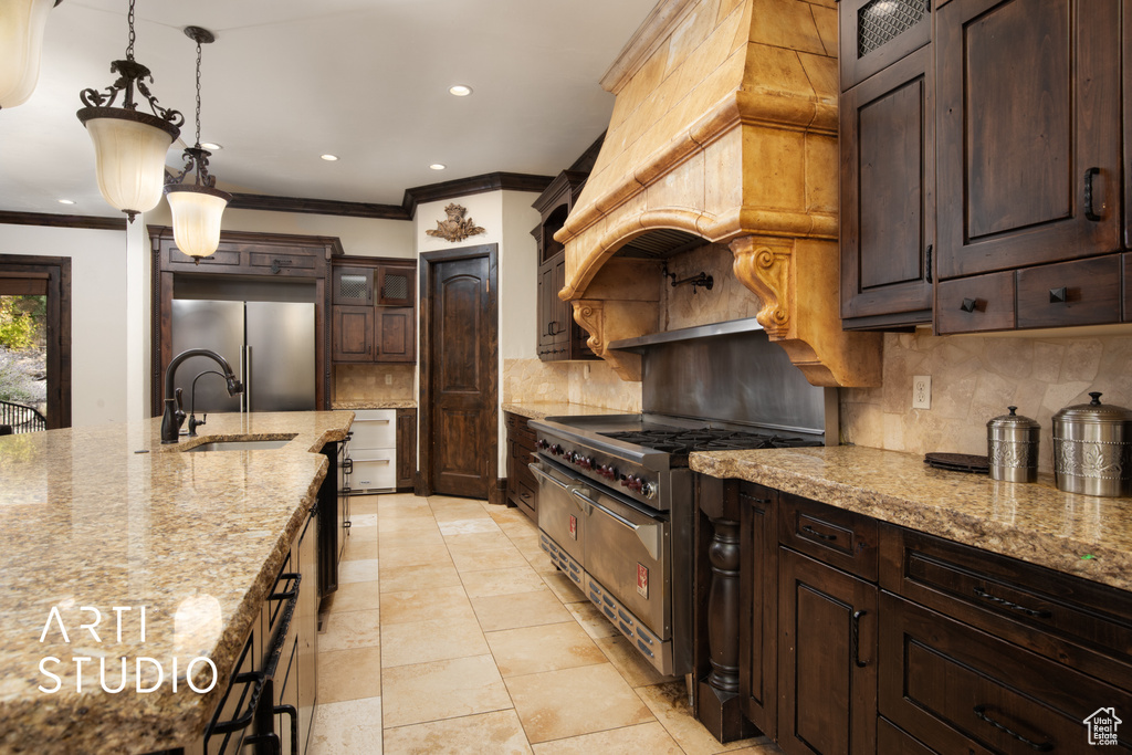 Kitchen with dark brown cabinetry, sink, stainless steel appliances, light stone countertops, and hanging light fixtures