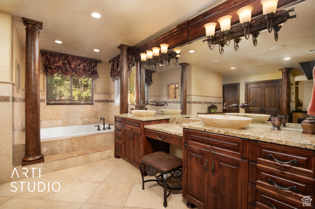 Bathroom featuring ornate columns, tile patterned flooring, tiled tub, and vanity