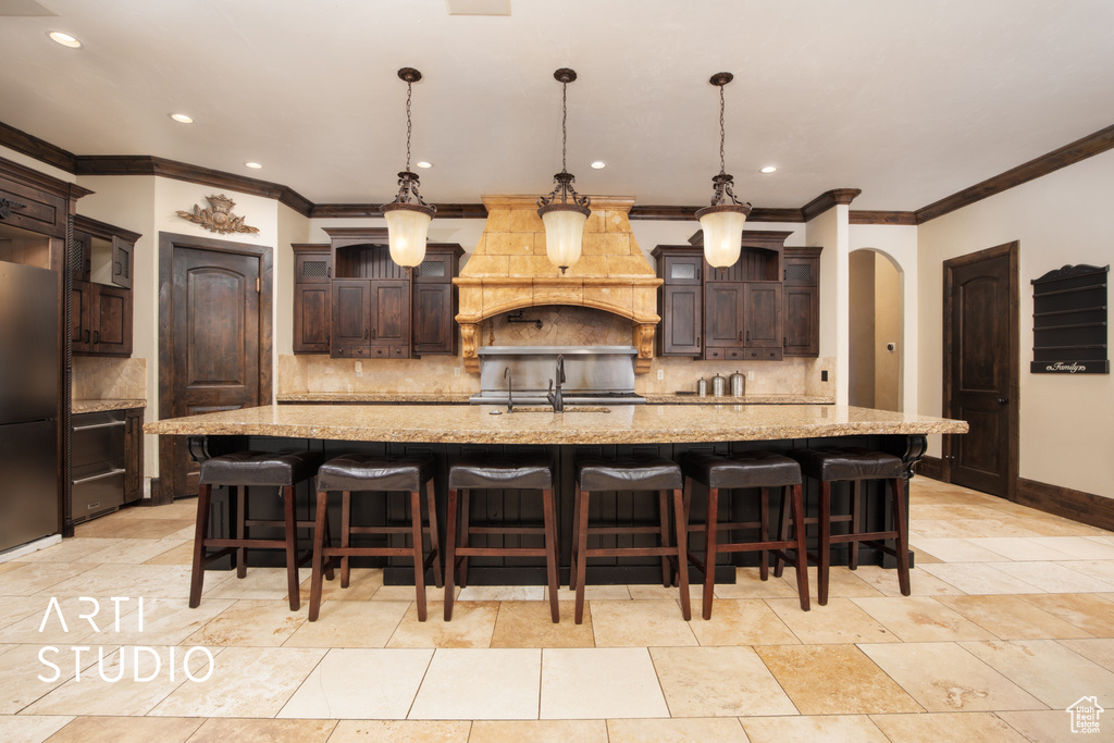 Kitchen featuring a large island with sink, dark brown cabinets, hanging light fixtures, and tasteful backsplash