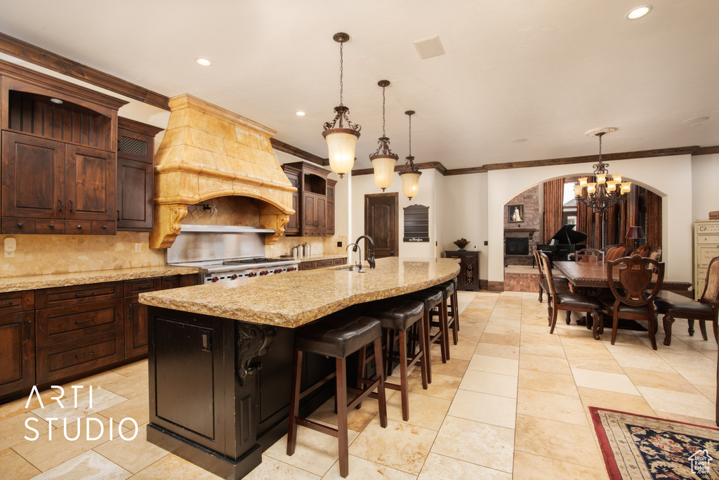 Kitchen featuring decorative light fixtures, a center island with sink, range, a kitchen breakfast bar, and custom range hood