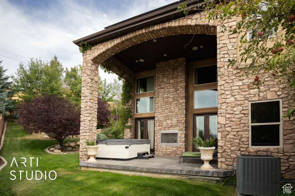 Rear view of property featuring cooling unit, a yard, and a hot tub