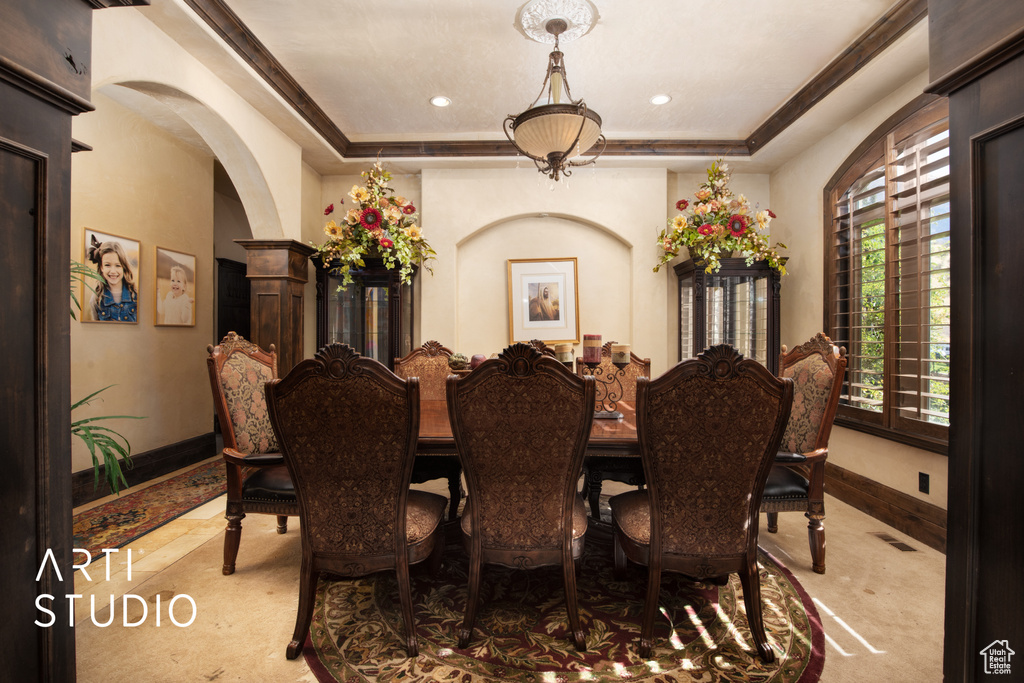 Dining area with a raised ceiling, crown molding, and light colored carpet