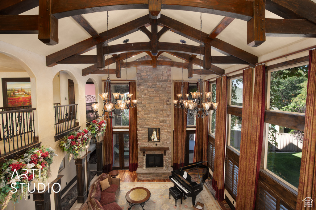 Living room featuring a stone fireplace, vaulted ceiling with beams, an inviting chandelier, and hardwood / wood-style floors