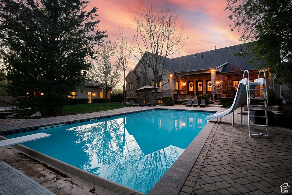 Pool at dusk featuring a diving board, a water slide, and a patio area