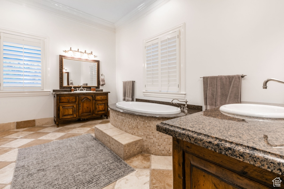 Bathroom with a relaxing tiled tub, vanity, tile patterned flooring, and ornamental molding