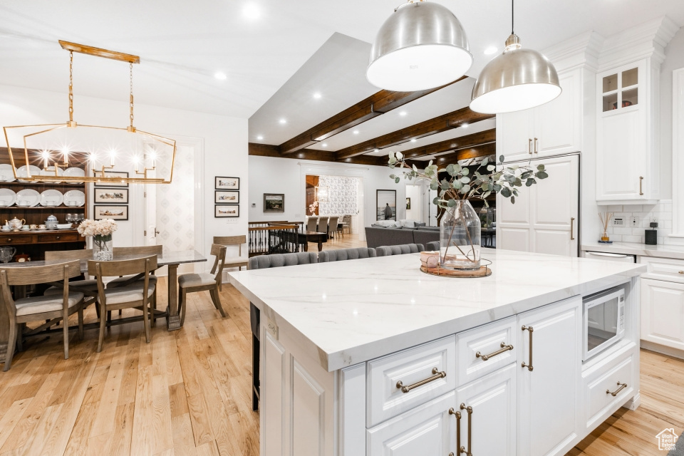 Kitchen featuring white microwave, beamed ceiling, light hardwood / wood-style floors, pendant lighting, and white cabinetry