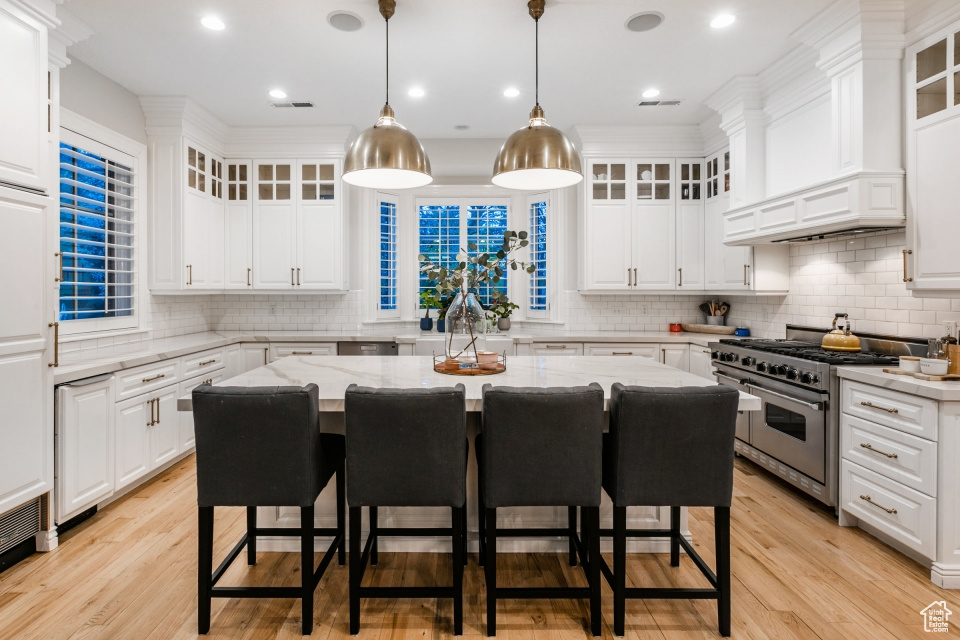 Kitchen with light wood-type flooring, high end range, a center island, and white cabinetry