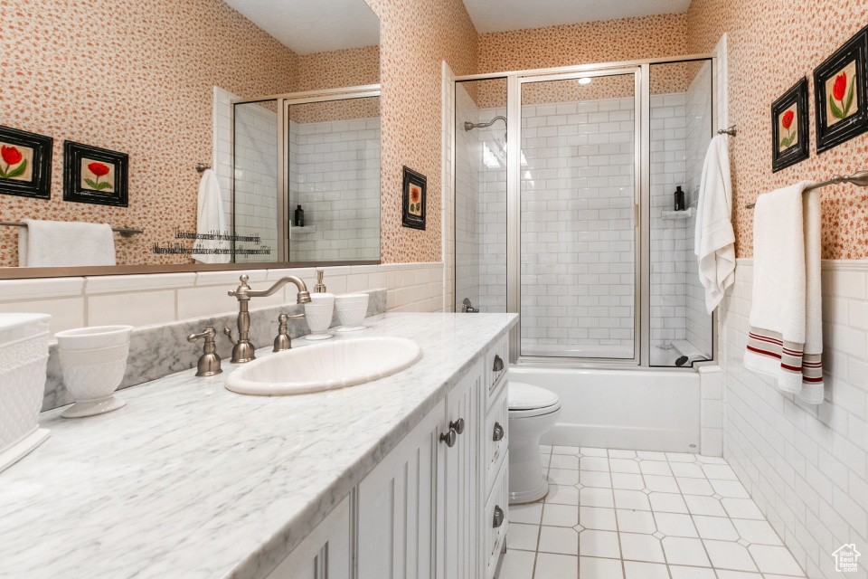 Full bathroom featuring tile patterned flooring, toilet, tile walls, bath / shower combo with glass door, and vanity