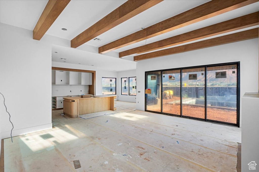 Unfurnished living room featuring plenty of natural light and beamed ceiling