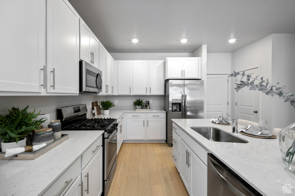 Kitchen with white cabinets, sink, appliances with stainless steel finishes, light stone countertops, and light hardwood / wood-style floors