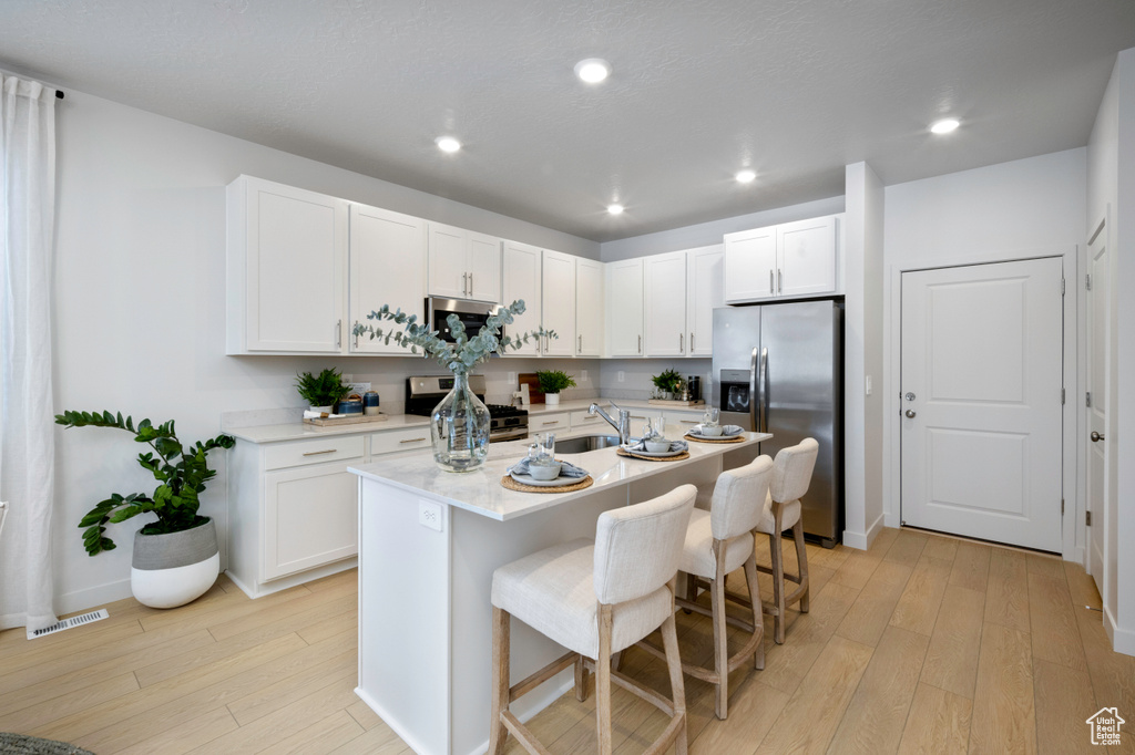 Kitchen featuring a breakfast bar area, light hardwood / wood-style flooring, stainless steel appliances, an island with sink, and white cabinets