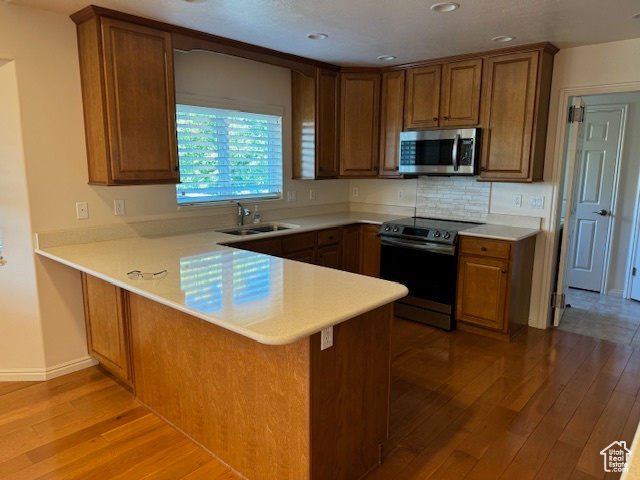 Kitchen featuring light wood-type flooring, black / electric stove, sink, kitchen peninsula, and backsplash