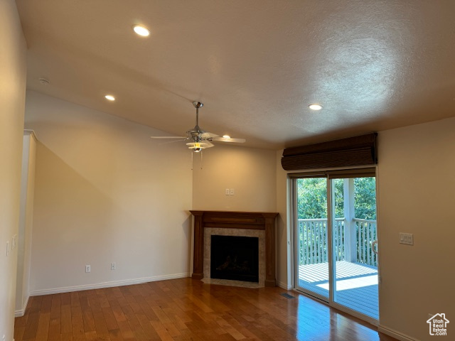 Unfurnished living room featuring ceiling fan, hardwood / wood-style flooring, a tiled fireplace, and a textured ceiling