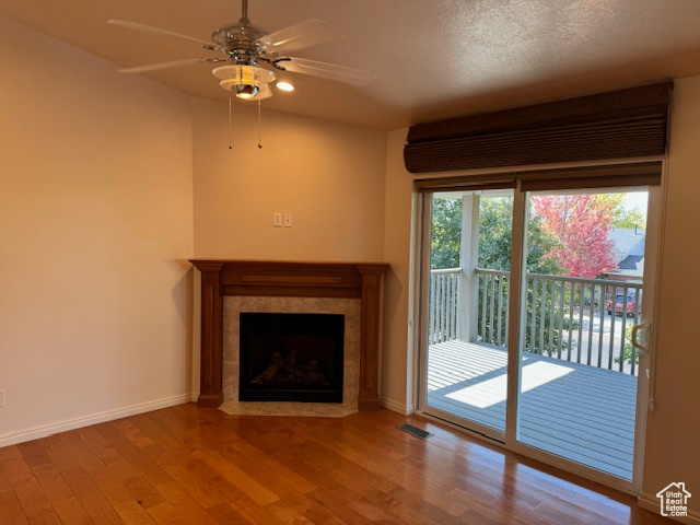 Unfurnished living room with ceiling fan, hardwood / wood-style flooring, a textured ceiling, and a tile fireplace