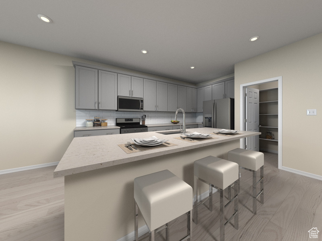 Kitchen featuring sink, a center island with sink, appliances with stainless steel finishes, light hardwood / wood-style floors, and decorative backsplash