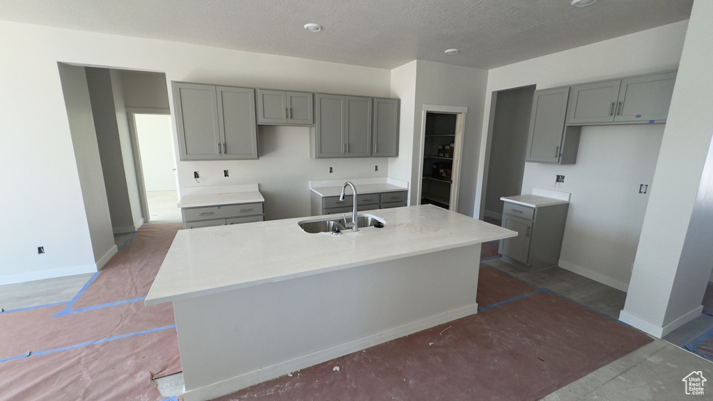 Kitchen with an island with sink, sink, gray cabinetry, and a textured ceiling