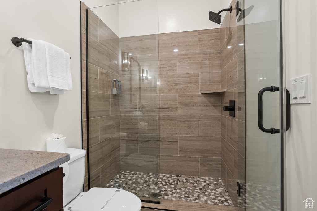 Bathroom featuring a shower with door, vanity, and toilet