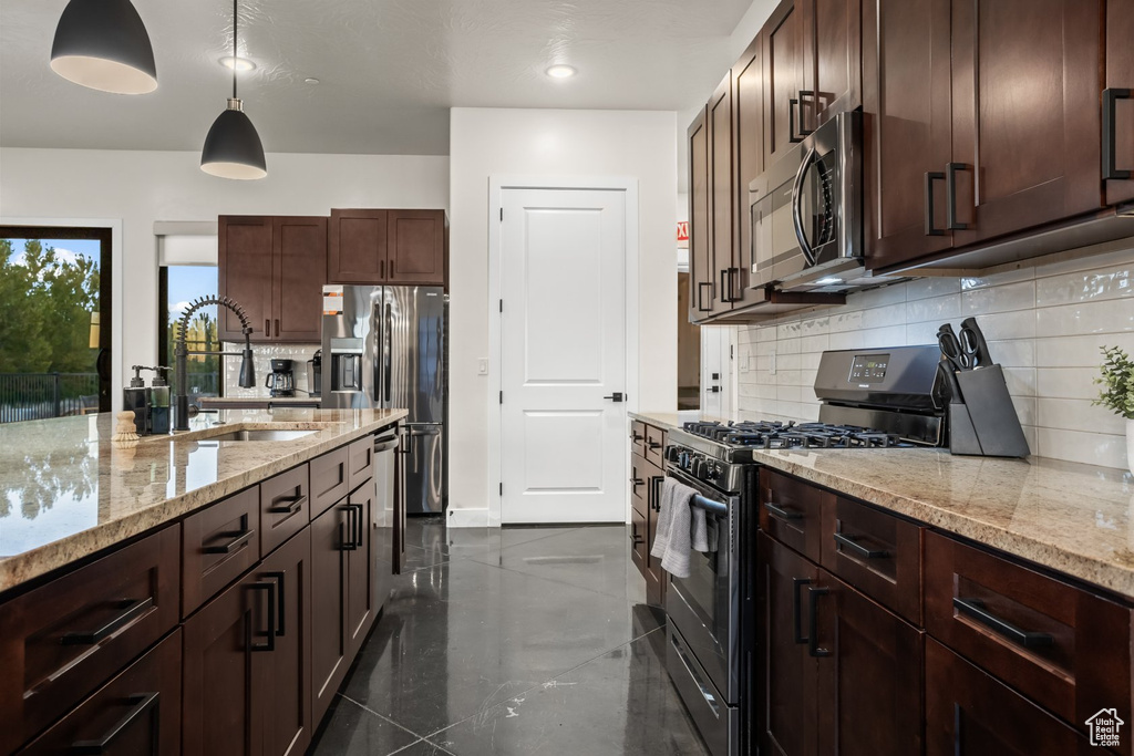 Kitchen featuring light stone countertops, stainless steel appliances, tasteful backsplash, sink, and pendant lighting