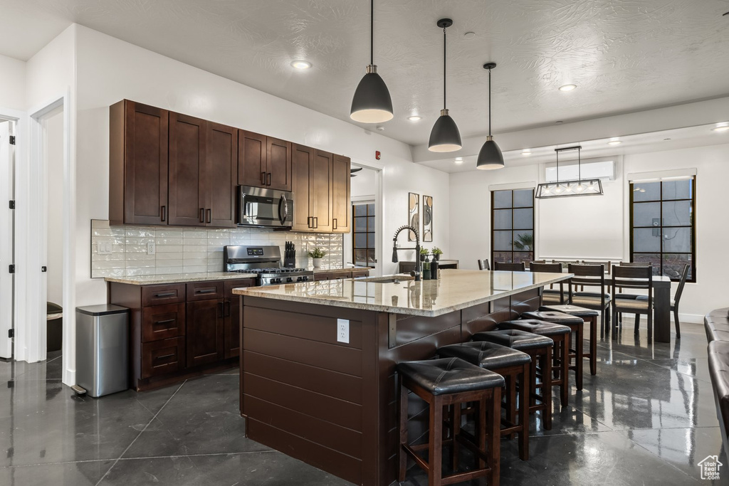 Kitchen with stainless steel appliances, an island with sink, decorative light fixtures, and a textured ceiling