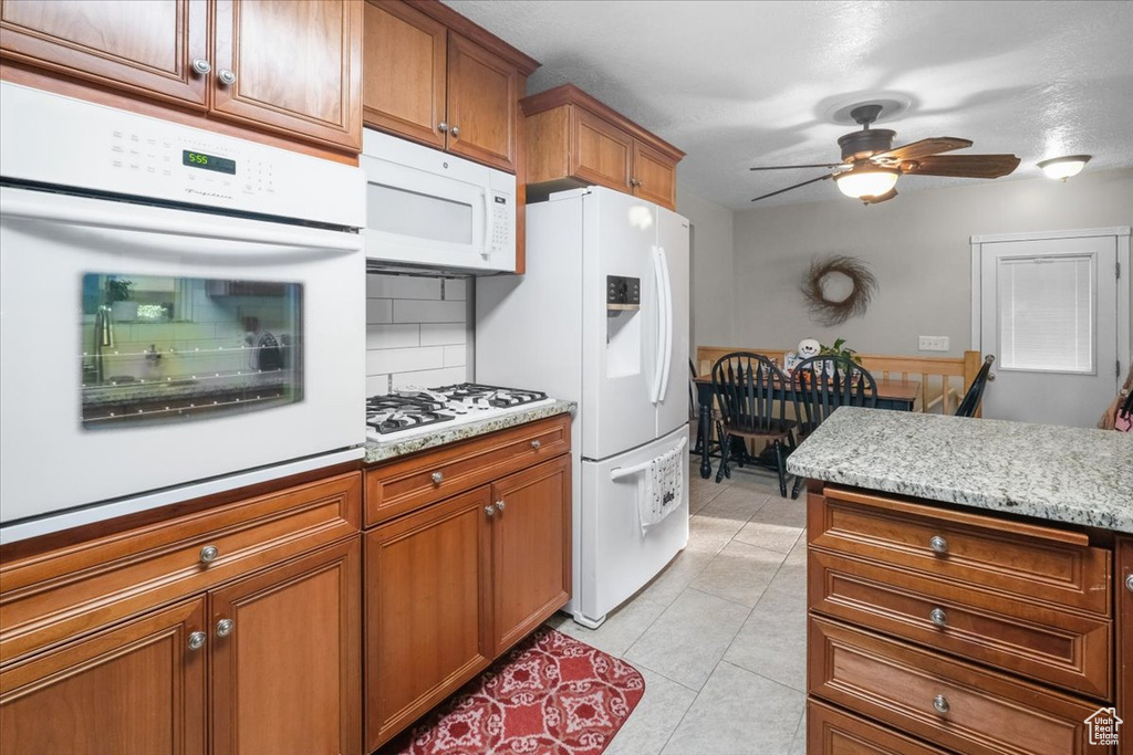 Kitchen with ceiling fan, light tile patterned floors, white appliances, tasteful backsplash, and light stone countertops