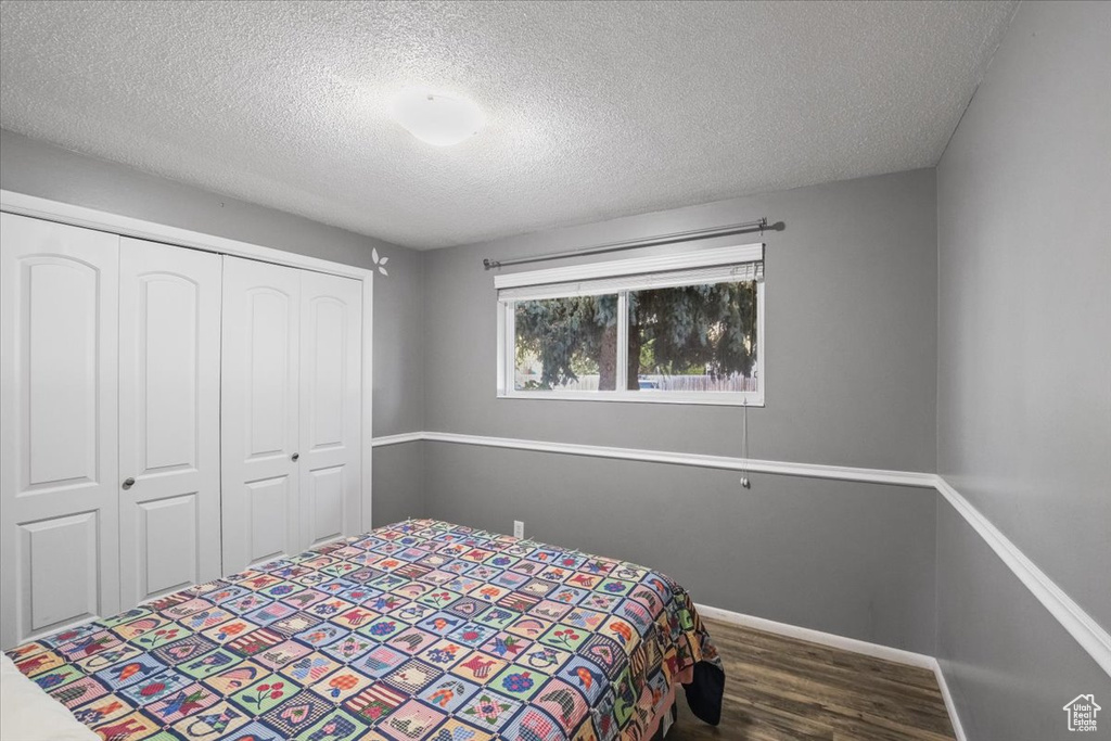 Bedroom with a textured ceiling, a closet, and dark hardwood / wood-style flooring