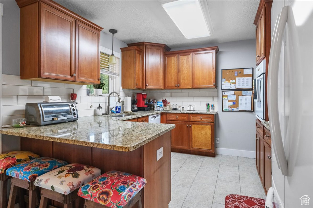 Kitchen with hanging light fixtures, kitchen peninsula, sink, white appliances, and a breakfast bar