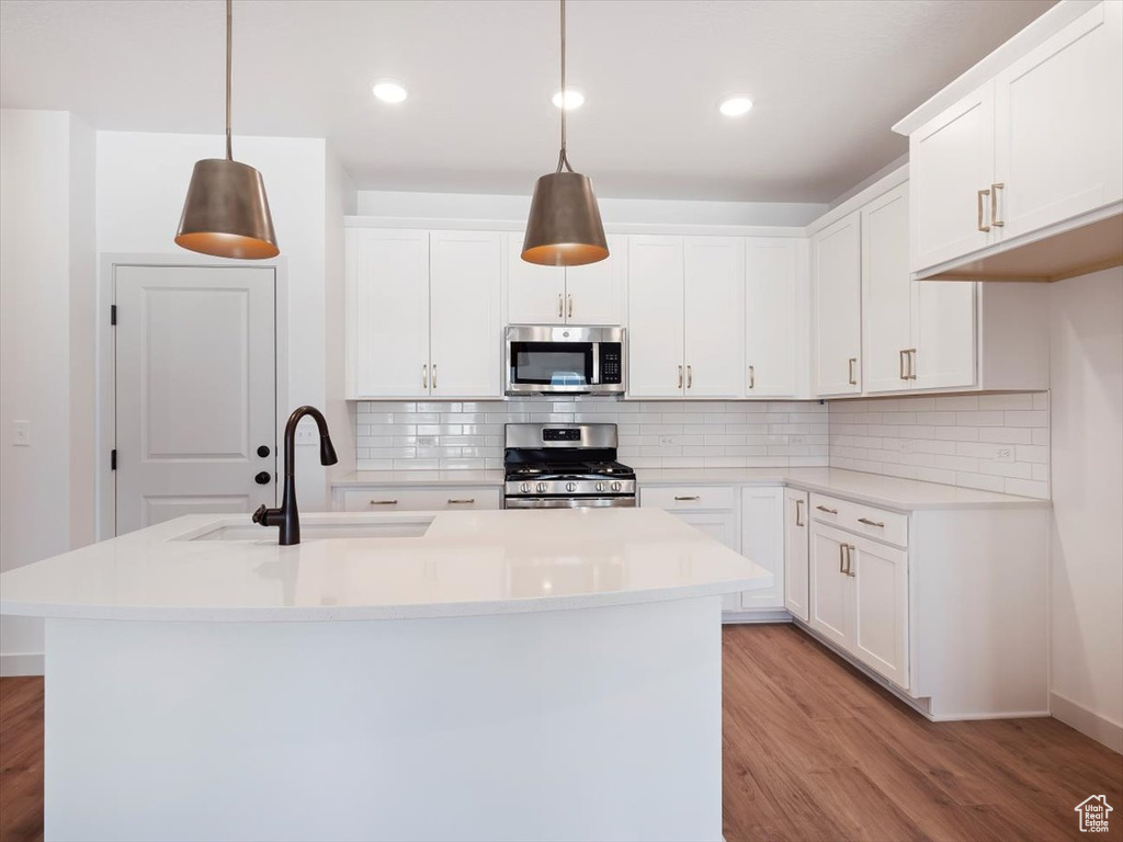 Kitchen featuring hanging light fixtures, sink, stainless steel appliances, and white cabinets