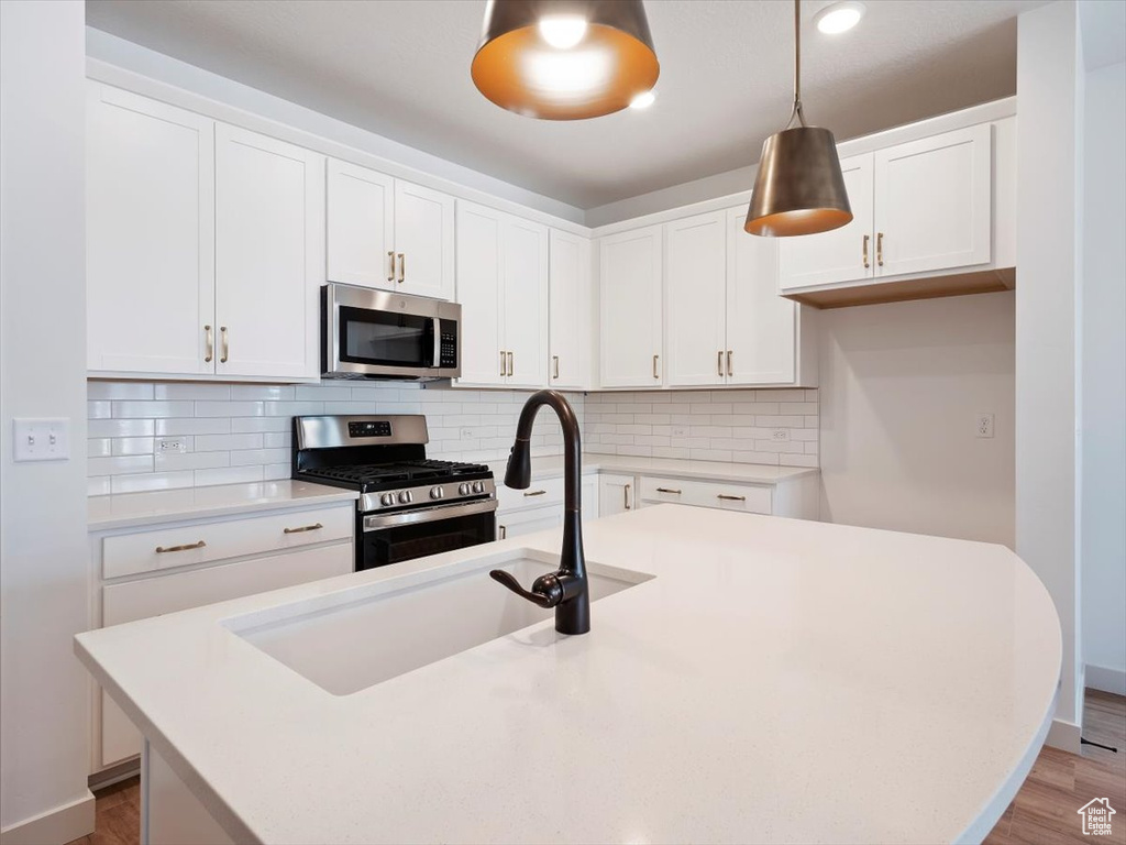 Kitchen with white cabinets, a kitchen island with sink, appliances with stainless steel finishes, and hanging light fixtures