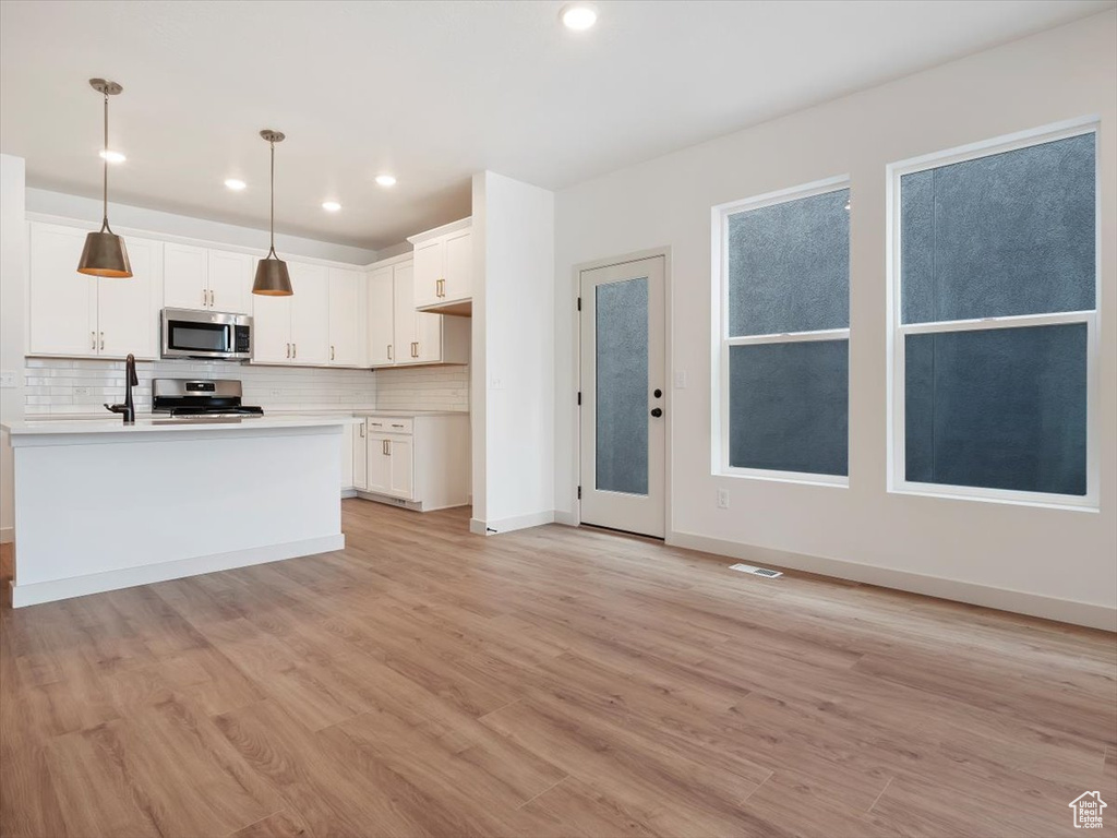 Kitchen with a kitchen island with sink, light wood-type flooring, hanging light fixtures, white cabinets, and appliances with stainless steel finishes