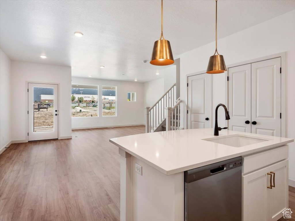 Kitchen featuring white cabinets, sink, stainless steel dishwasher, decorative light fixtures, and light hardwood / wood-style floors